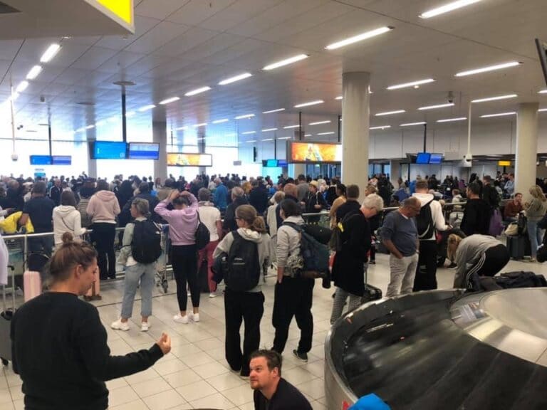 Drukte op Schiphol bij bagageband, honderden mensen bij elkaar